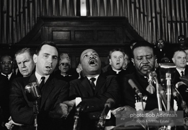 King leads the singing of “We Shall Overcome” after eulogizing a slain civil rights crusader, the Reverend James Reeb, Brown Chapel, Selma, Alabama. 1965.
