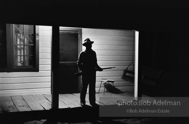 Reverend Carter, expecting a visit from the Klan after he has dared to register to vote, stands guard on his front porch,  West Feliciana Parish, Louisiana. 1964-


“After Reverend Carter had registered to vote, that night vigilant neighbors scattered in the woods near his farmhouse, which was at the end of a long dirt road, to help him if trouble arrived. ‘If they want a fight, we’ll fight,’ Joe Carter told me. ‘If I have to die, I’d rather die for right.’ “He told me, ‘I value my life more since I became a registered voter. A man is not a first-class citizen, a number one citizen, unless he is a voter.’ After Election Day came and went, Reverend Carter added, ‘I thanked the Lord that he let me live long enough to vote.’”
