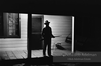 Reverend Carter, expecting a visit from the Klan after he has dared to register to vote, stands guard on his front porch,  West Feliciana Parish, Louisiana. 1964-


“After Reverend Carter had registered to vote, that night vigilant neighbors scattered in the woods near his farmhouse, which was at the end of a long dirt road, to help him if trouble arrived. ‘If they want a fight, we’ll fight,’ Joe Carter told me. ‘If I have to die, I’d rather die for right.’ “He told me, ‘I value my life more since I became a registered voter. A man is not a first-class citizen, a number one citizen, unless he is a voter.’ After Election Day came and went, Reverend Carter added, ‘I thanked the Lord that he let me live long enough to vote.’”