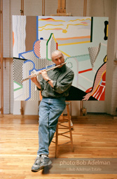 Roy Lichtenstein plays his flute while sitting in front of his painting Interior with Woman Leaving. 1997.-photo©Bob Adelman, artwork ©Estate of Roy Lichtenstein
