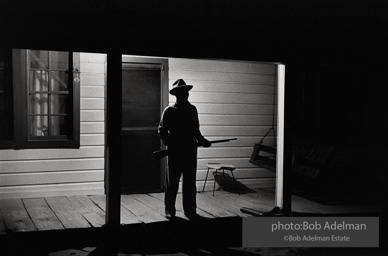 Reverend Carter, expecting a visit from the Klan after he has dared to register to vote, stands guard on his front porch, West Feliciana Parish, Louisiana. 1964
“After Reverend Carter had registered to vote, that night vigilant neighbors scattered in the woods near his farmhouse, which was at the end of a long dirt road, to help him if trouble arrived. ‘If they want a fight, we’ll fight,’ Joe Carter told me. ‘If I have to die, I’d rather die for right.’ “He told me, ‘I value my life more since I became a registered voter. A man is not a first-class citizen, a number one citizen, unless he is a voter.’ After Election Day came and went, Reverend Carter added, ‘I thanked the Lord that he let me live long enough to vote. Reverend Carter, expecting a visit from the Klan after he has dared to register to vote, stands guard on his front porch, West Feliciana Parish, Louisiana. 1964
“After Reverend Carter had registered to vote, that night vigilant neighbors scattered in the woods near his farmhouse, which was at the end of a long dirt road, to help him if trouble arrived. ‘If they want a fight, we’ll fight,’ Joe Carter told me. ‘If I have to die, I’d rather die for right.’ “He told me, ‘I value my life more since I became a registered voter. A man is not a first-class citizen, a number one citizen, unless he is a voter.’ After Election Day came and went, Reverend Carter added, ‘I thanked the Lord that he let me live long enough to vote.