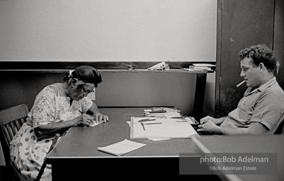 A elderly woman attempts to complete complex voter registration form in order to qualify to vote. She is overseen by a registrar. That summer groups like Core, SNCC, and the SCLC made an attempt to register large numbers of black voters in the deep south. Freedom Summer, voter registration. Louisiana,1964.