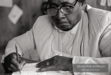 Elderly woman is practicing filling out voter registration form in the Core office in Sumpter, South Carolina. She repeatedly practiced to get the correct answers, and earlier failed attempt is crushed in her hand. Later that day she went to City Hall and succesfully competed the form and was registered to vote. Sumpter, South Carolina, 1962.