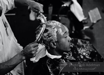 Styling: A barber conks, or chemically straightens, his client’s hair, New York City.  1962