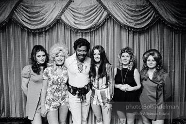 “Silky,” a pimp, with his “stars,” New York City.  1970


“Why would a pimp who leeches off women end up as a popular culture hero? The illusion persists that there is
some effortless way to make it to Easy Street. And in a world of one-parent families, a man who is getting it
over on women may appear enviable. Outlaws can look like heroes to the young and rebellious. Maybe that’s why a good deal of the pimp’s lingo and myth and style permeates hip-hop. This isn’t brand new: Americans have been for generations listening to music, dancing, dressing and talking with expressions that started on the
street. Jazz was first played in bordellos, jitterbugging and zoot suits came up from the underground. Chump
change, a Wall Street expression, originally referred to the kind of money an unsuccessful pimp made.”
