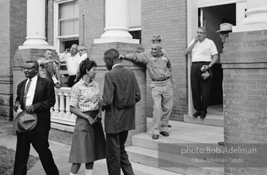 After eight years of trying, the Reverend Joe Carter succeeds in registering to vote then is jeered as he walks down the courthouse steps,  St. Francisville,  Louisiana.  1964

“Joe Carter was the first African American in his parish to register to vote in the twentieth century — this despite the fact that two out of three residents of the parish were black. Once he succeeded in his quest, danger was in the air. I remember someone at the courthouse shouting at me, ‘Take his picture, it may be the last one he takes.’”