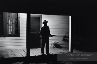 Reverend Carter, expecting a visit from the Klan after he has dared to register to vote, stands guard on his front porch,  West Feliciana Parish, Louisiana. 1964-


“After Reverend Carter had registered to vote, that night vigilant neighbors scattered in the woods near his farmhouse, which was at the end of a long dirt road, to help him if trouble arrived. ‘If they want a fight, we’ll fight,’ Joe Carter told me. ‘If I have to die, I’d rather die for right.’ “He told me, ‘I value my life more since I became a registered voter. A man is not a first-class citizen, a number one citizen, unless he is a voter.’ After Election Day came and went, Reverend Carter added, ‘I thanked the Lord that he let me live long enough to vote.’”