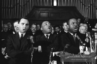 King leads the singing of “We Shall Overcome” after eulogizing a slain civil rights crusader, the Reverend James Reeb, Brown Chapel,  Selma,  Alabama.  1965