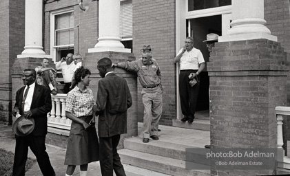 After eight years of trying, the Reverend Joe Carter succeeds in registering to vote then is jeered as he walks down the courthouse steps,  St. Francisville,  Louisiana.  1964

“Joe Carter was the first African American in his parish to register to vote in the twentieth century — this despite the fact that two out of three residents of the parish were black. Once he succeeded in his quest, danger was in the air. I remember someone at the courthouse shouting at me, ‘Take his picture, it may be the last one he takes.’”