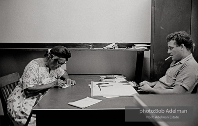 Registrar of Voters observing woman filling out a voter registration form, Clinton, East Feliciana Parish, LA 1964. Prospective registrants were not allowed to receive any help in filling out registration forms and had to complete
them in a specified amount of time with only the registrar present in the room. Even the smallest mistake provided
grounds to reject an application.