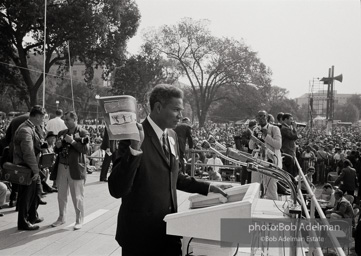 Ossie Davis, MC, at the assembly point near the Washington Mounument holds up the official poster for the March with Bob Adelman's Water Hosing photograph. August 28, 1963.