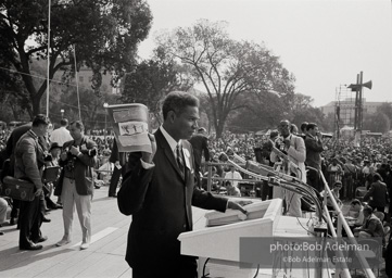 Ossie Davis, MC, at the assembly point near the Washington Mounument holds up the official poster for the March with Bob Adelman's Water Hosing photograph. August 28, 1963. Ossie Davis, MC, at the assembly point near the Washington Mounument holds up the official poster for the March with Bob Adelman's Water Hosing photograph. August 28, 1963.
