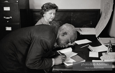Man signing his registration certificate in the Registrar of Voters’ office after successfully registering to vote,
Sumter SC 1962. The registrar of voters had the power to accept or reject applications and there were varying degrees of cooperation
or hostility in different districts. Adelman found that in Sumter, the voter registration officers were less
intimidating than in the Felicianas in Louisiana Man signing his registration certificate in the Registrar of Voters’ office after successfully registering to vote,
Sumter SC 1962. The registrar of voters had the power to accept or reject applications and there were varying degrees of cooperation
or hostility in different districts. Adelman found that in Sumter, the voter registration officers were less
intimidating than in the Felicianas in Louisiana