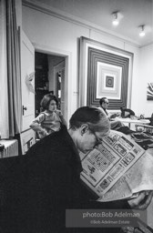 Andy Warhol reads the small ads in the Village Voice (Kay Bearman and Ivan Karp in background). Leo Castelli Gallery. New York City, 1965.