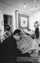 Andy Warhol reads the small ads in the Village Voice (Kay Bearman and Ivan Karp in background). Leo Castelli Gallery. New York City, 1965.