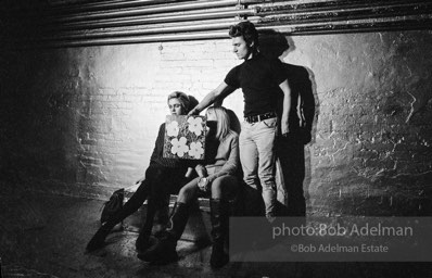 Gerard Malanga taking a light reading
using Flowers on the set of Prison. Edie Sedgwick and Bibbe Hanson (seated).The Factory, 1965.