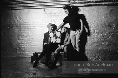 Gerard Malanga taking a light reading
using Flowers on the set of Prison. Edie Sedgwick and Bibbe Hanson (seated).The Factory, 1965.