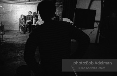 Andy Warhol (in the shadows) while filming a scene for the film Prison (aka Girls in Prison). Bibbe Hanson, Edie Sedgwick and Pat Hartley seated. The Factory, 1965.