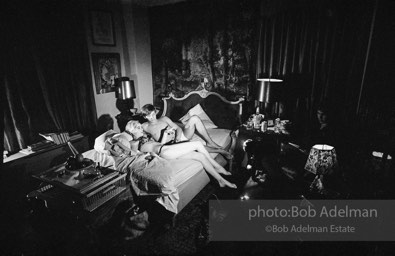 During Beauty #2, Edie Sedgwick answers questions from Chuck Wein off-camera in the shadows  while grappling with Gino Piserchio on the bed. New York City apartment, 1965.