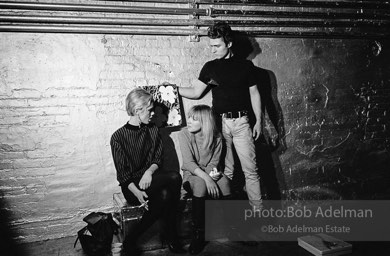 Gerard Malanga taking a light reading
using Flowers on the set of Prison. Edie Sedgwick and Bibbe Hanson (seated).The Factory, 1965.