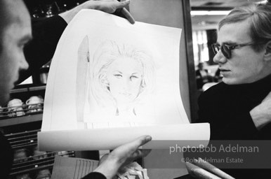 An artist shows Andy a drawing of Baby Jane Holzer as a matchbook cover in a mid-town restaurant. New York City, 1965.