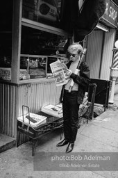 Andy Warhol reads the New York Times ouside a news stand. 1965.